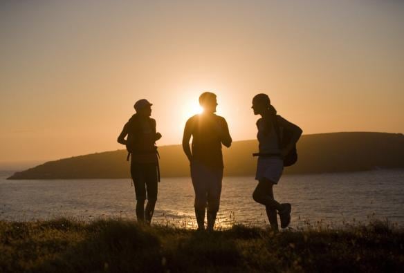 Three people hiking with backpacks as the sun sets over the ocean at Kings Head, Fleurieu Peninsula,  South Australia © South Australian Tourism Commission/Peter Fisher
