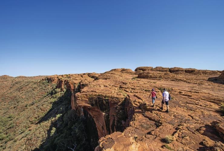 Two people walking close to a cliff edge with bushland below along the Rim Walk, Kings Canyon, Northern Territory © Tourism Northern Territory/Shaana McNaught 