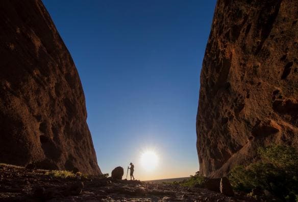 A person standing between two rocky cliffs as the sun begins to set along the Valley of the Winds walk, Kata Tjuta, Red Centre, Northern Territory © Tourism NT, Sean Scott