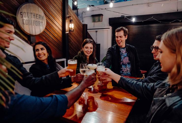 A group of people raising cocktails and glasses of beer around a wooden table in a dimly lit venue. with Local Sauce Tours, Sydney, New South Wales © Local Sauce Tours