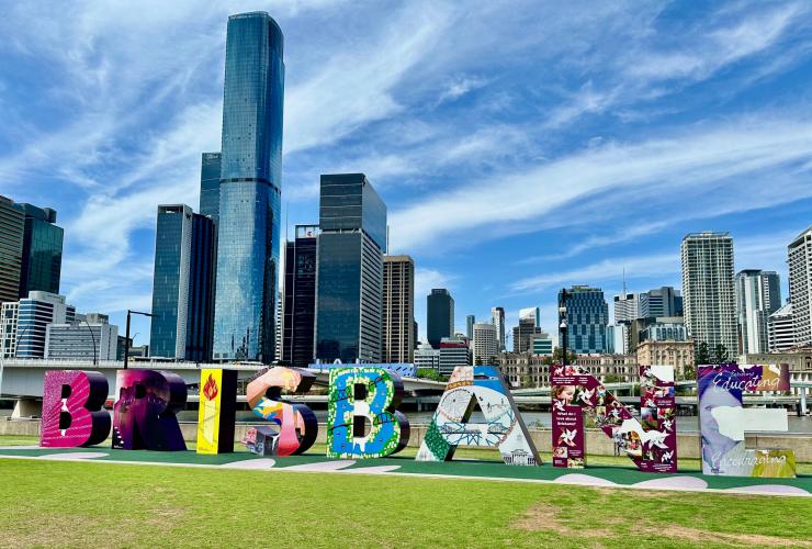A large sign reading "Brisbane" on a grassy field in front of a city skyline during a tour with Urban Tours, Brisbane, Queensland © Urban Tours