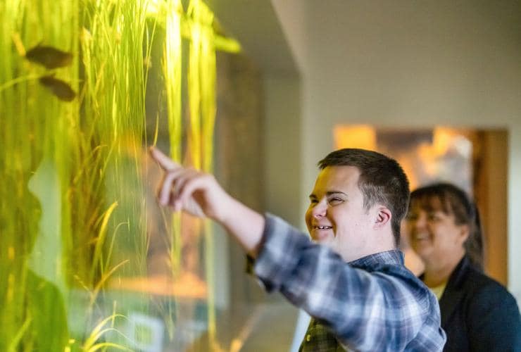 A man with neurodivergence pointing towards a tank enclosure with a woman standing beside him at Alice Springs Desert Park, Alice Springs, Northern Territory © Tourism NT/Helen Orr