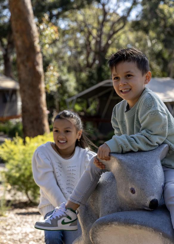 Hai em bé chơi với một tác phẩm điêu khắc hình gấu koala, Khu bảo tồn gấu koala Port Stephens, Port Stephens, Tiểu bang New South Wales © Tourism Australia 