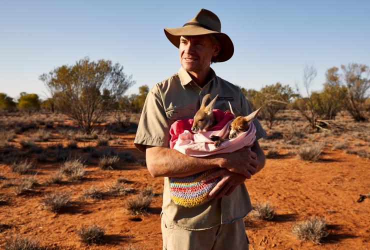 A guide holding two kangaroo joeys at The Kangaroo Sanctuary, Alice Springs, Northern Territory © Tourism Australia