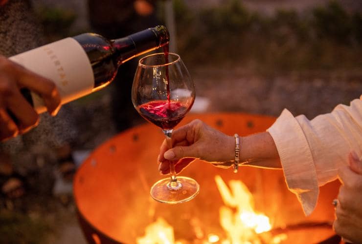 Red wine pouring into a glass with a bonfire in the background at Ubertas Wines, Barossa, South Australia © Tourism Australia