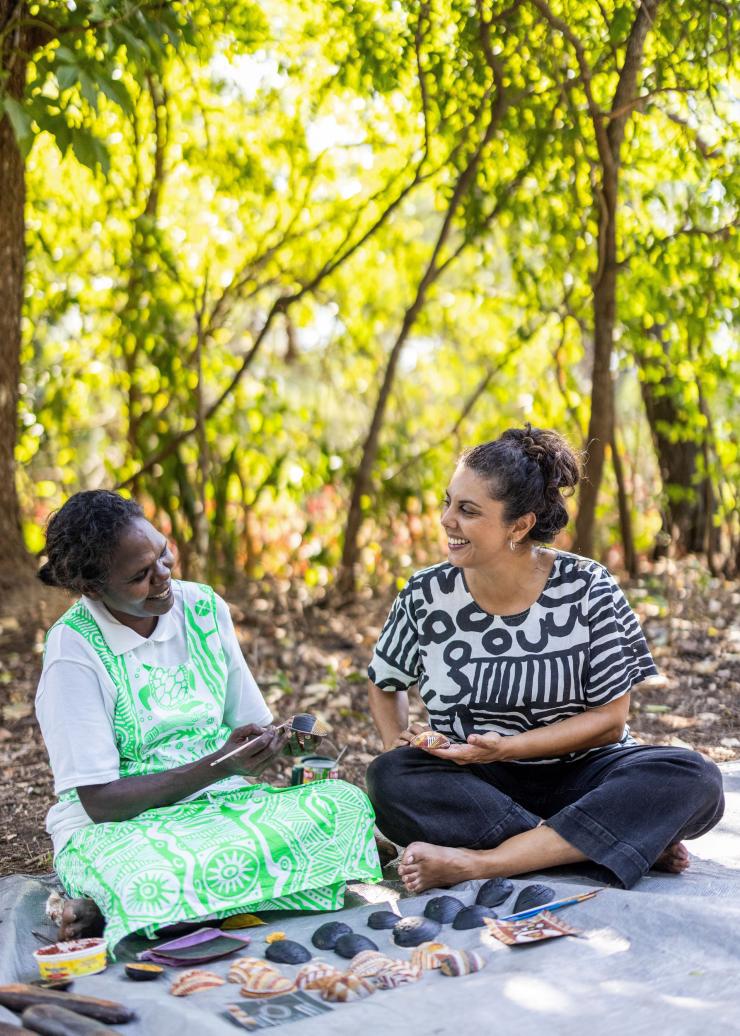 A woman sits with an Indigenous local as she paints shells on a Tiwi Islands Cultural Tour, Tiwi Islands, Northern Territory © Tourism NT