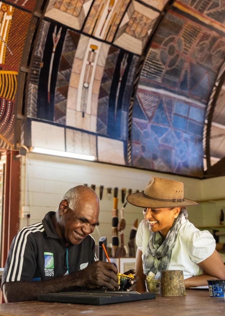 A local artist and visitor laugh together as the artist paints at Ngaruwanajirri Art Centre, Tiwi Islands, Northern Territory © Tourism NT/Helen Orr 