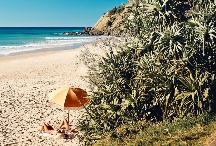 Two people laying on the sand under a beach umbrella in Byron Bay, New South Wales © Sydney Bespoke Tours 