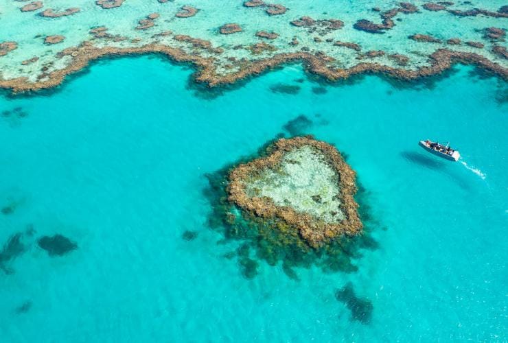 An aerial view of a reef in the ocean shaped like a heart with a boat alongside, Heart Reef, Whitsundays, Queensland © Tourism and Events Queensland