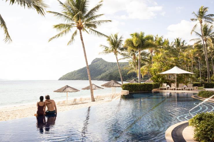 A couple sits on the edge of an infinity pool overlooking the ocean on Hamilton Island, Whitsundays, Queensland © Tourism Australia