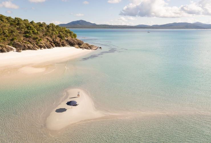 An aerial view of a couple sitting on an empty white sand cay surrounded by blue ocean in the Whitsundays, Queensland © Tourism Australia