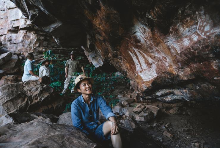 A visitor smiles as they look at Aboriginal art painted on a cave wall with Kakadu Cultural Tours, Kakadu National Park, Northern Territory © Tourism Australia