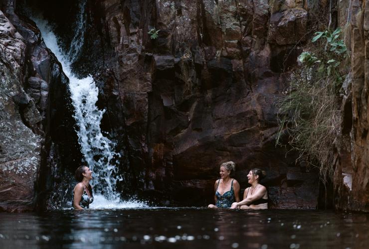 Three women sit in the water below a waterfall at Ikoymarrwa (Moline) Falls, Kakadu National Park, Northern Territory © Tourism Australia 