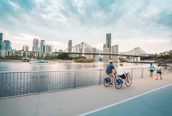 Hai người đạp xe dọc theo con sông chảy qua thành phố, Đường đi bộ ven sông, Thành phố Brisbane, Tiểu bang Queensland © Tourism and Events Queensland