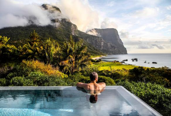 一名男子在新南威爾士州豪勳爵島（Lord Howe Island）卡佩拉酒店（Capella Lodge）無邊泳池中眺望擁有翠綠美景的海濱景觀©Baillie Lodges