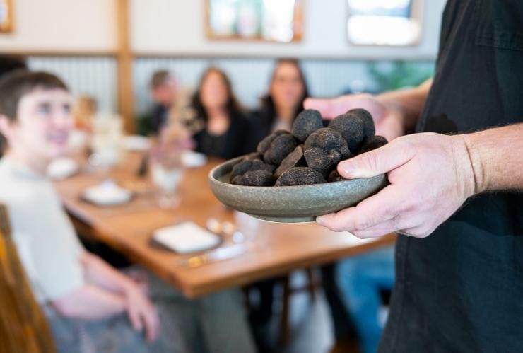 澳洲首都領地馬德拉松露農場內一個人捧著一碟松露走向一枱食客©澳洲旅遊局