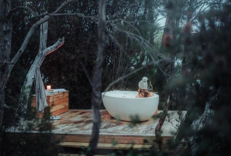 塔斯曼尼亞聖佳爾湖泵房角The Retreat度假屋內一位女士正在享用藏於樹叢中的戶外浴缸©Emilie Ristevski