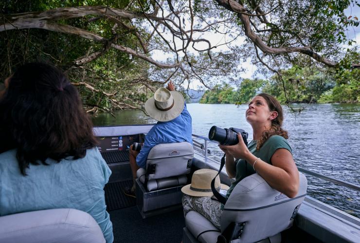 昆士蘭州戴恩樹Daintree Boatman Wildlife Cruises的觀光船正沿著寧靜的水道前行，船上一人拿著相機，周圍是雨林©澳洲旅遊局